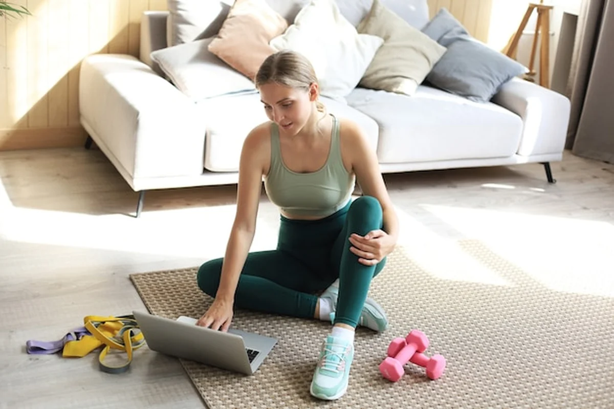Kobieta w stroju sportowym z hantlami i laptopem w salonie